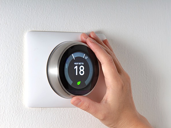 Hand adjusting a heating thermostat with temperature displayed as 18